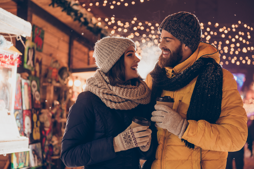 A couple bundled up and drinking hot drinks as they shop at an outdoor holiday market