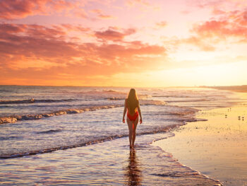 photo of a girl in a red bathing suit walking along the shore at sunset