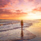 photo of a girl in a red bathing suit walking along the shore at sunset