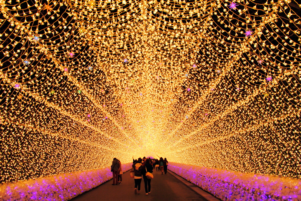 A tunnel covered in white and purple lights with people walking through it. 