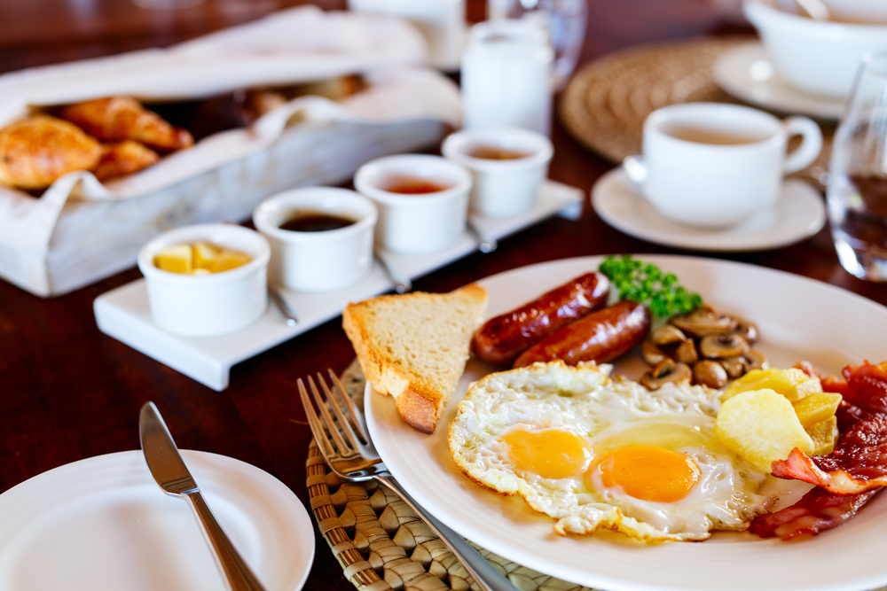 a delicious eggs over easy, sausage, bacon, mushroom with toast and assortment of jams and coffee