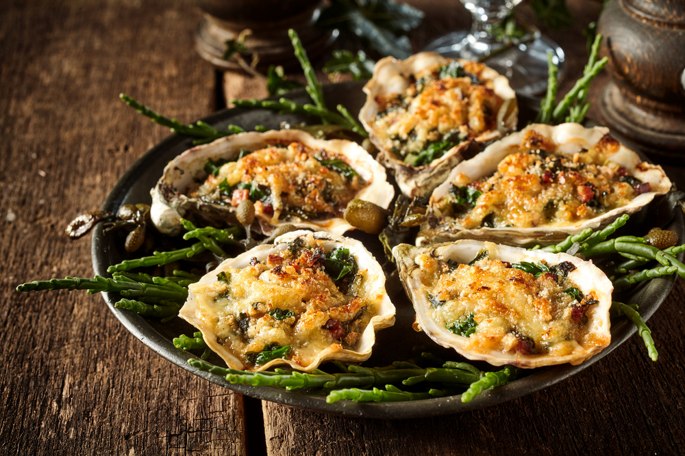 a plate of grilled oysters topped with cheese and herbs