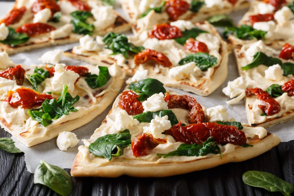 a pizza with hummus base topped with sun dried totes and cheese and basil