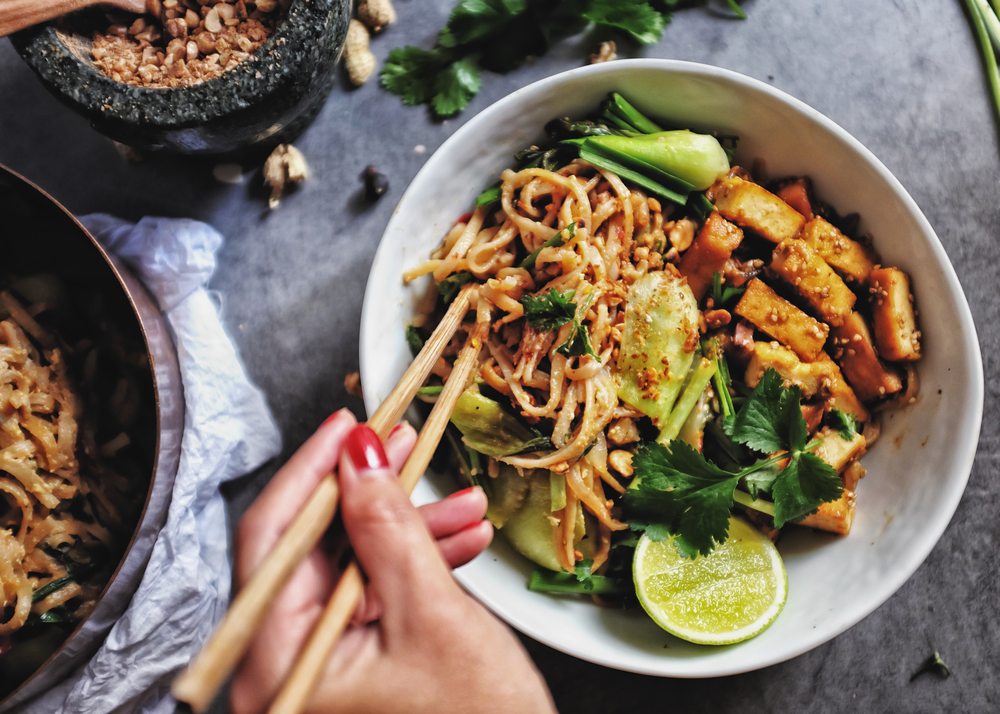 Tofu pad thai at one of the outer banks restaurants with a woman's hand holding chop sticks 