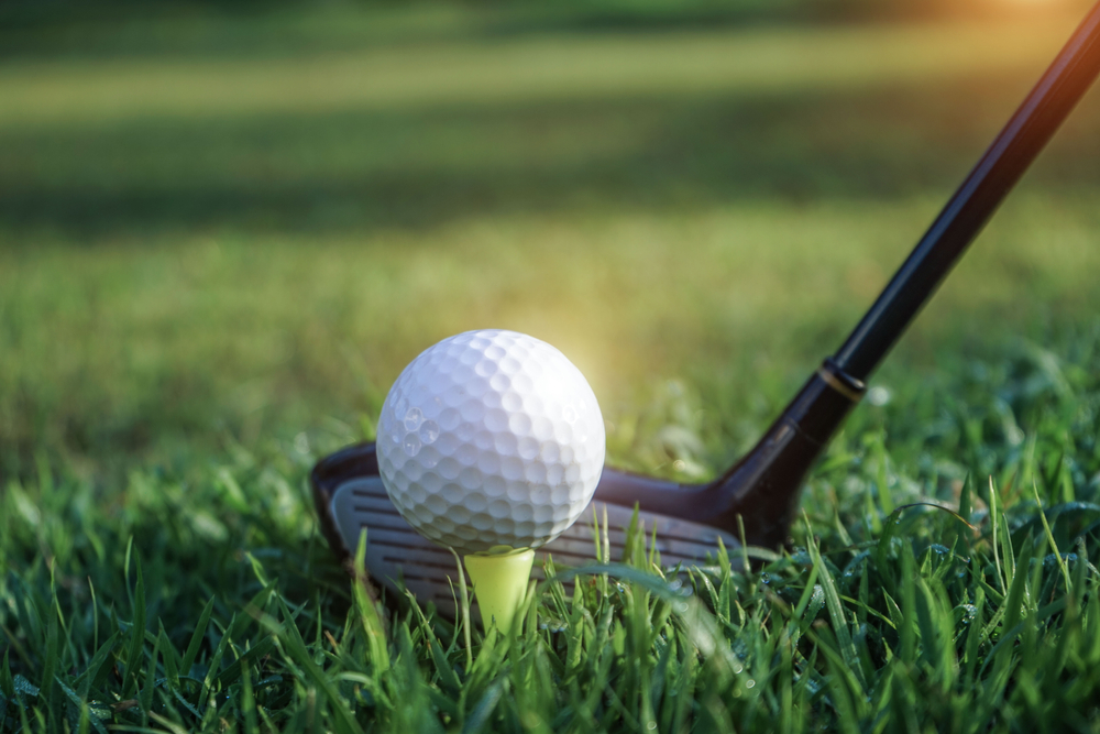 Golf club and golf ball close up in grass field with sunset. Golfing is one of the things to do in Duck.