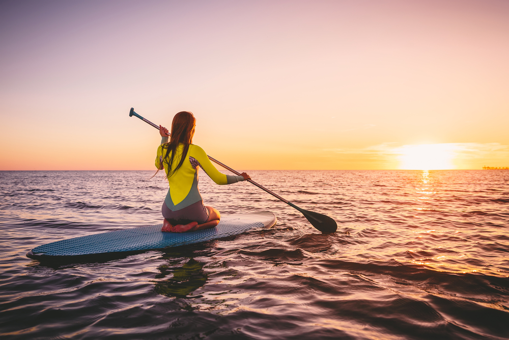 Girl on stand up paddle board, quiet sea with warm sunset colors.