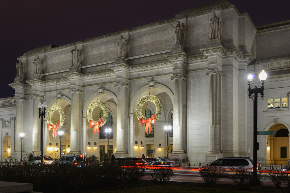 The front of Union Station in Washington DC with large wreaths lit up for Christmas at night. 