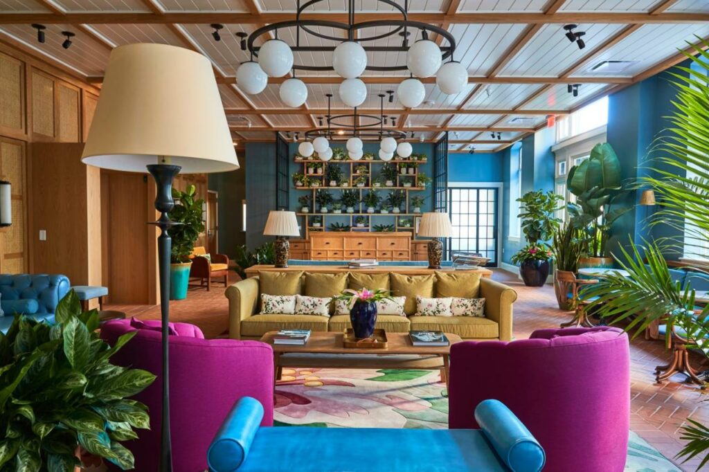 The colorful interior of a common area in the Drayton Hotel, one of the best boutique hotels in Savannah. There are many plants spread about the light and airy room with blue walls and modern lights.