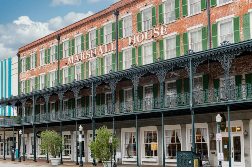 The brick exterior of the Marshall House, one of the best boutique hotels in Savannah, with its wrought-iron balconies and green shutters.