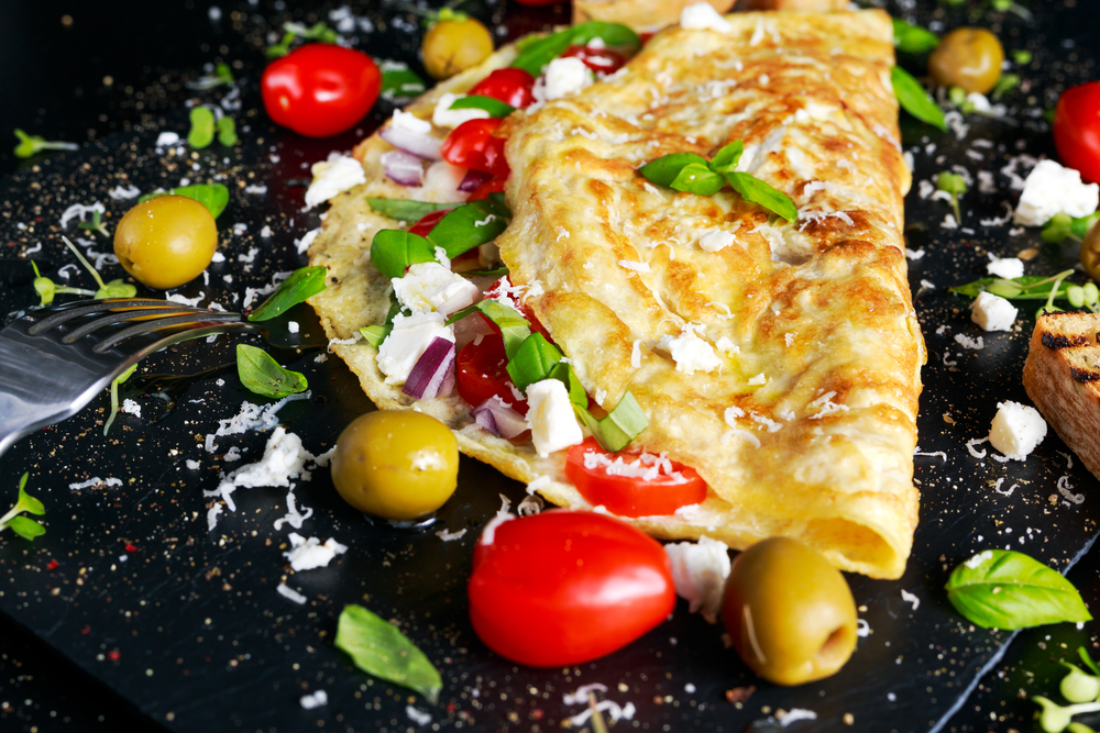 Close up of a folded omelette brimming with olives, feta and tomato. 
