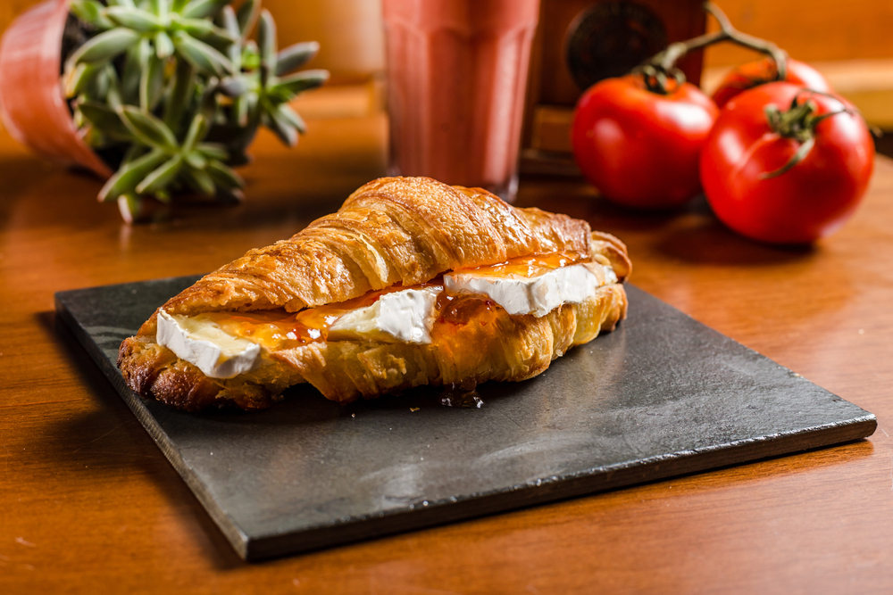 Close up photo of a croissant with brie and apricot preserve on a slate plate. 