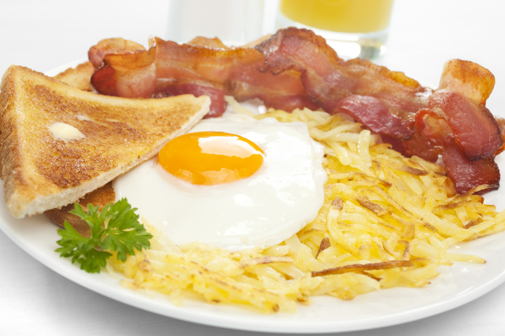 Fried egg on a plate of potato hash with buttered toast and bacon. 