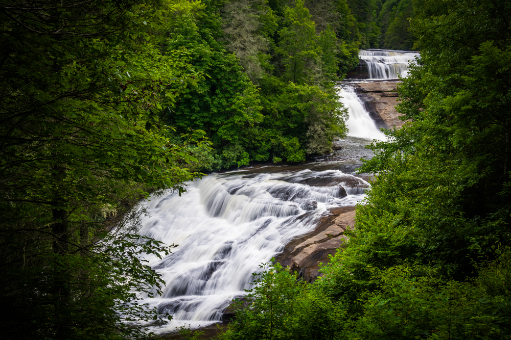 The three sections of Triple Falls flowing through green trees. 