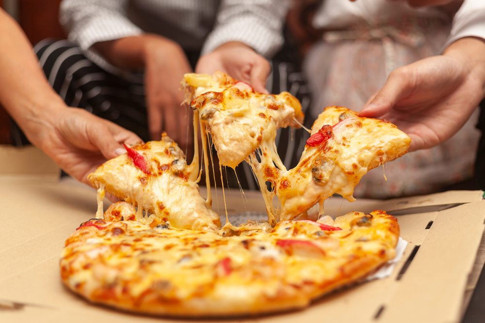 people grabbing pieces of pizza out of pizza box