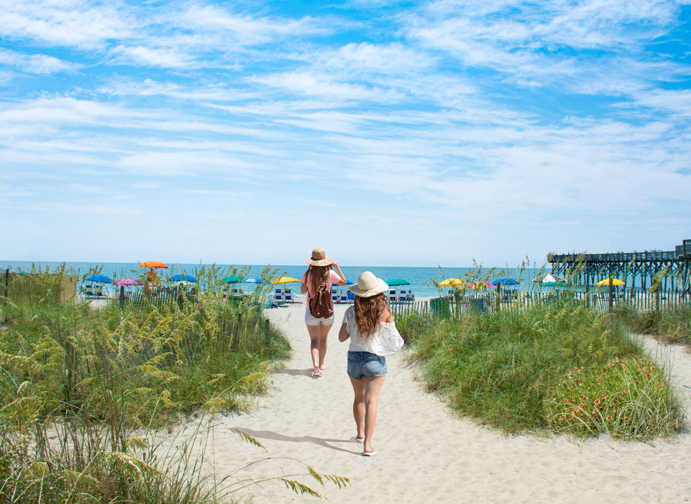 Girls walking on the beach on summer vacation. Beach chairs and parasols on beautiful white sand in the background. Going to the beach is one of the best things to do at Myrtle Beach