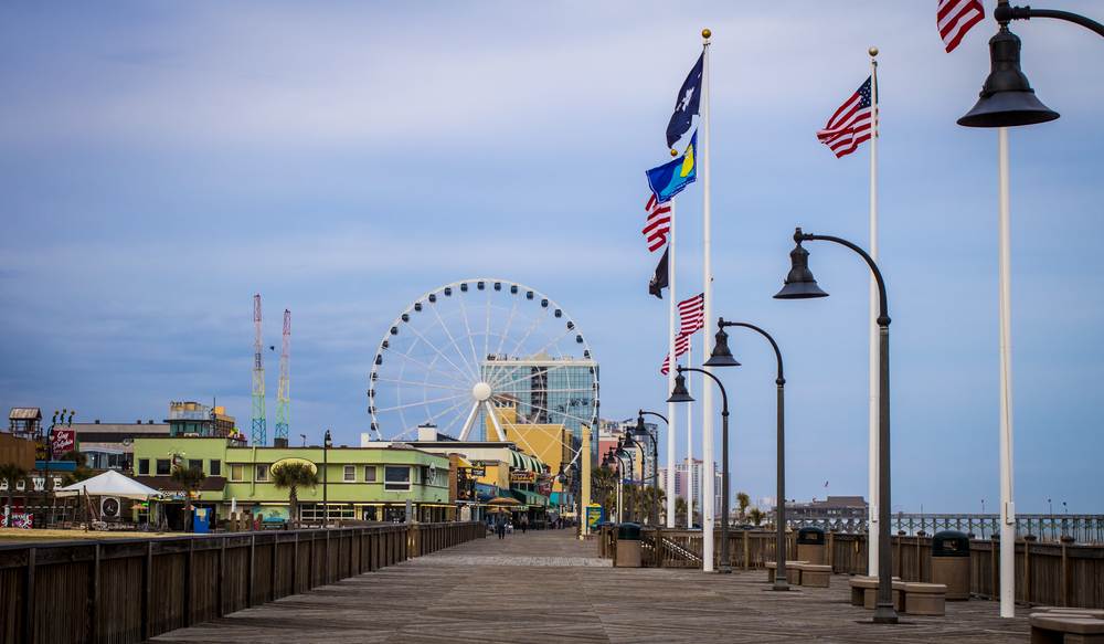  Myrtle Beach boardwalk showing the braodwalk and buildings and attractions. There are flags flying. 