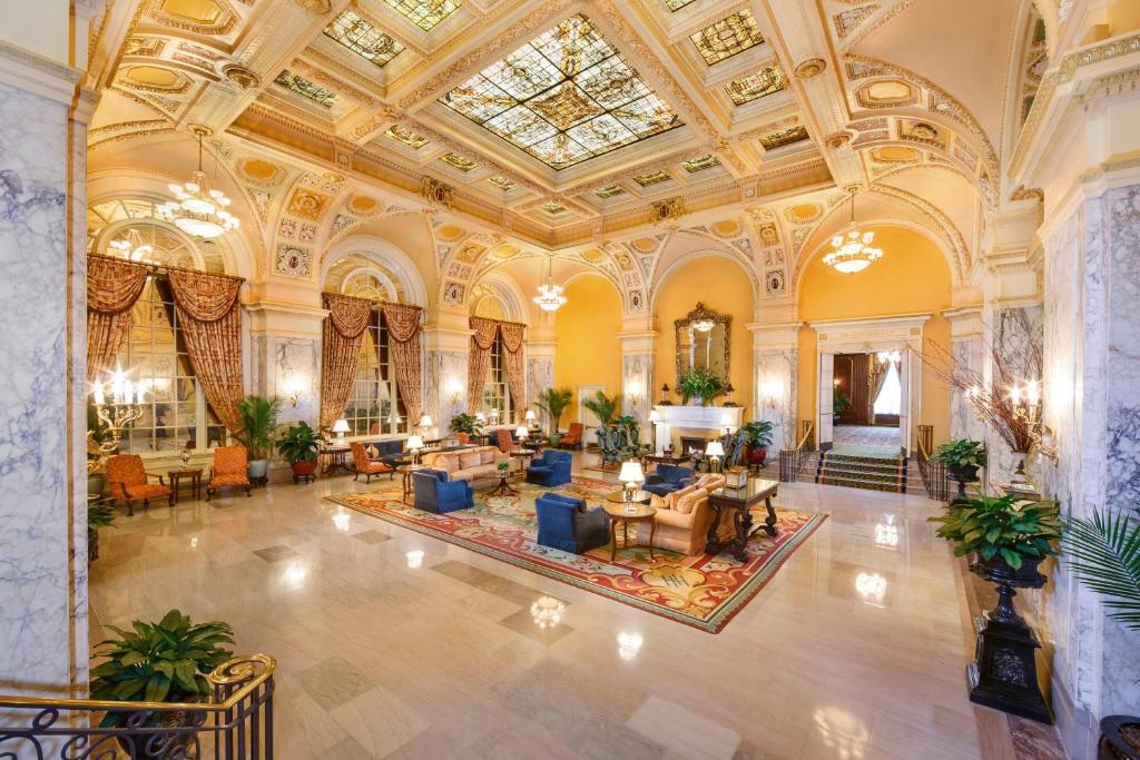 A grand lobby with an elegant celing and chairs and sofas in the middle. 