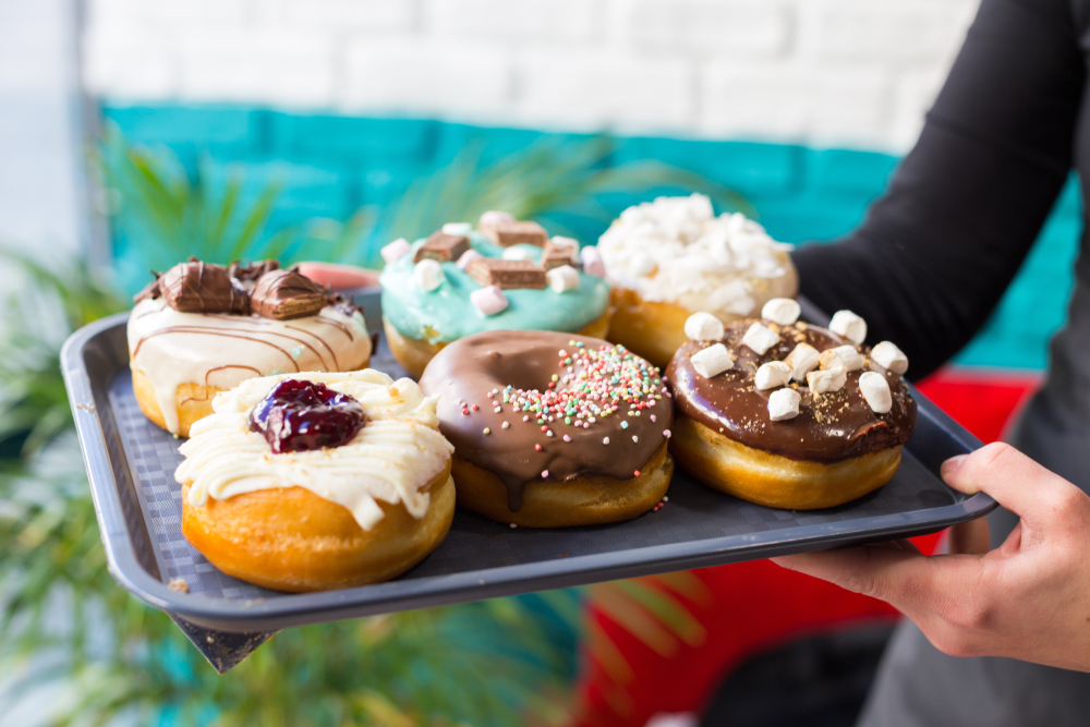 A person holding a tray of gourmet donuts with various toppings. 