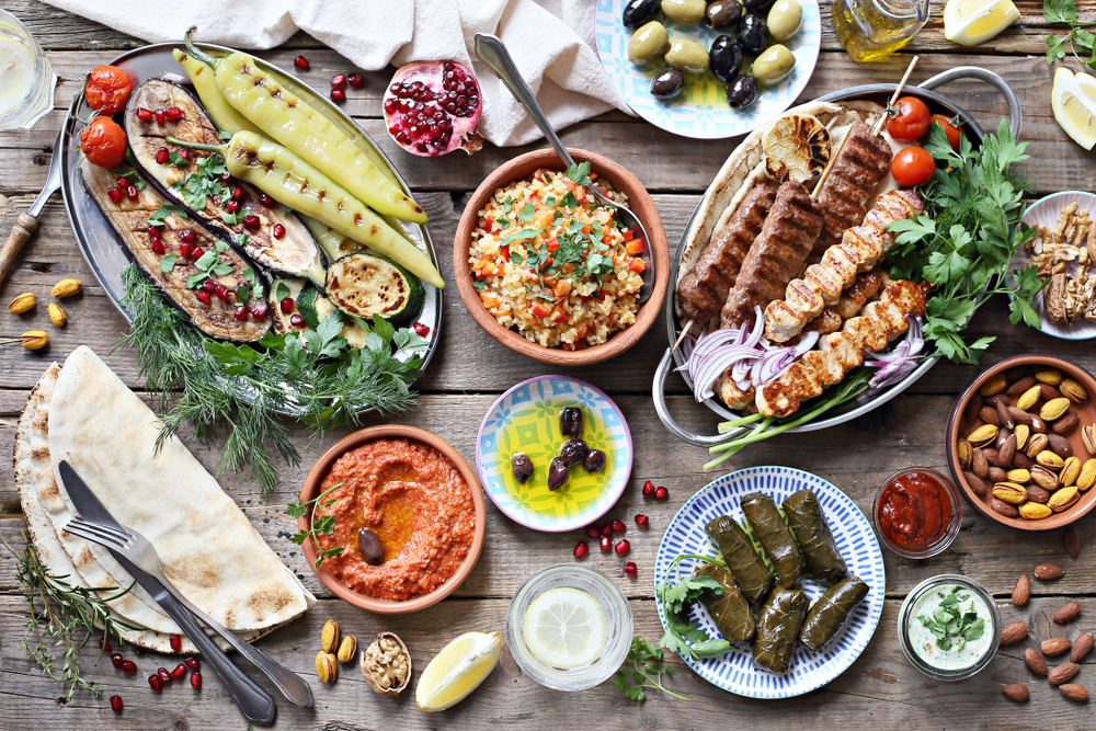 A massive spread of Mediterranean dishes like kabobs, grape leaves, pita, couscous, and vegetables. 