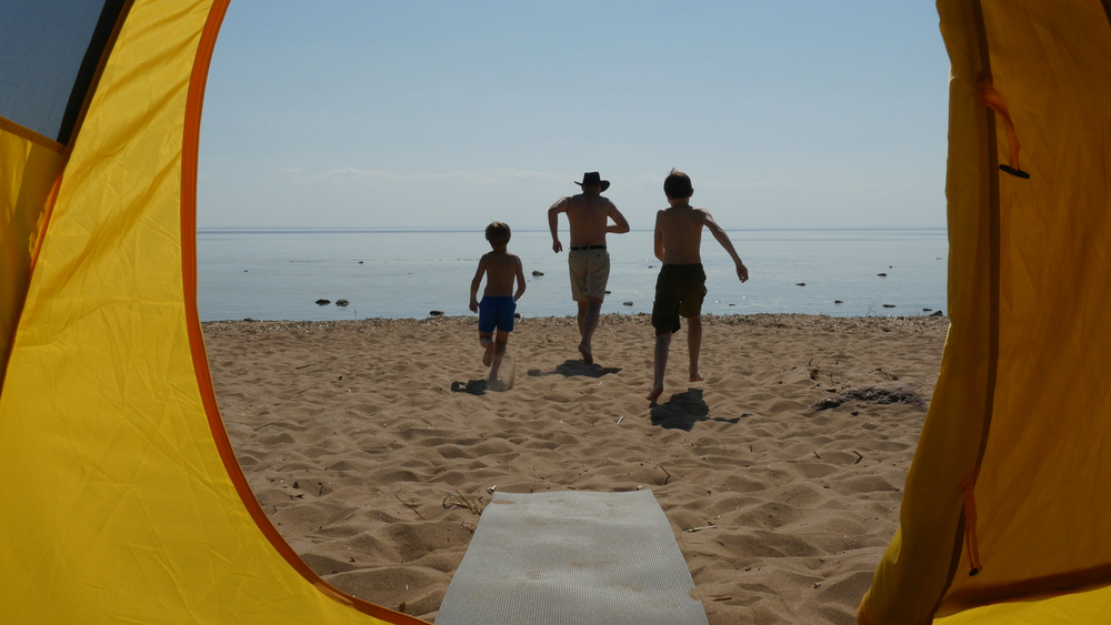 Photo of a tent on the beach and people running to the water. A common scene at Adventure Bound Campground, one of the best outer banks campgrounds. 