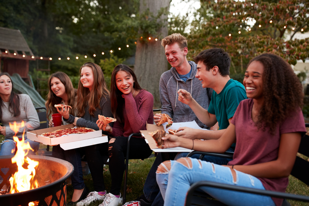 Photo of friends eating pizza around a campfire at KOA OBX, one of the best Outer Banks campgrounds