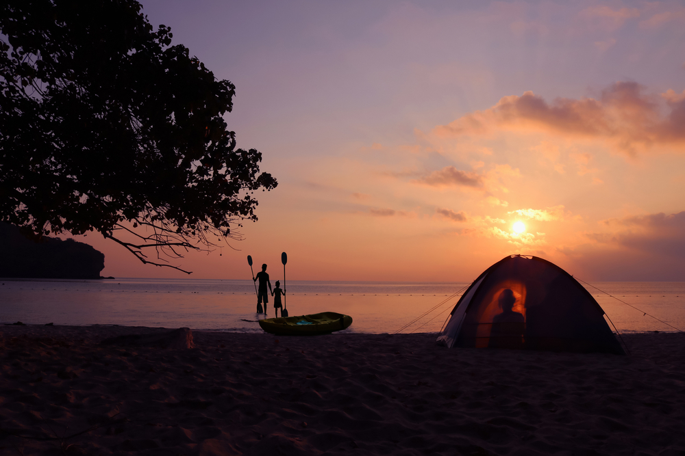 Photo of a beach sunset at St. Clair Landing with a tent on the beach and an adult and child wading in the water.