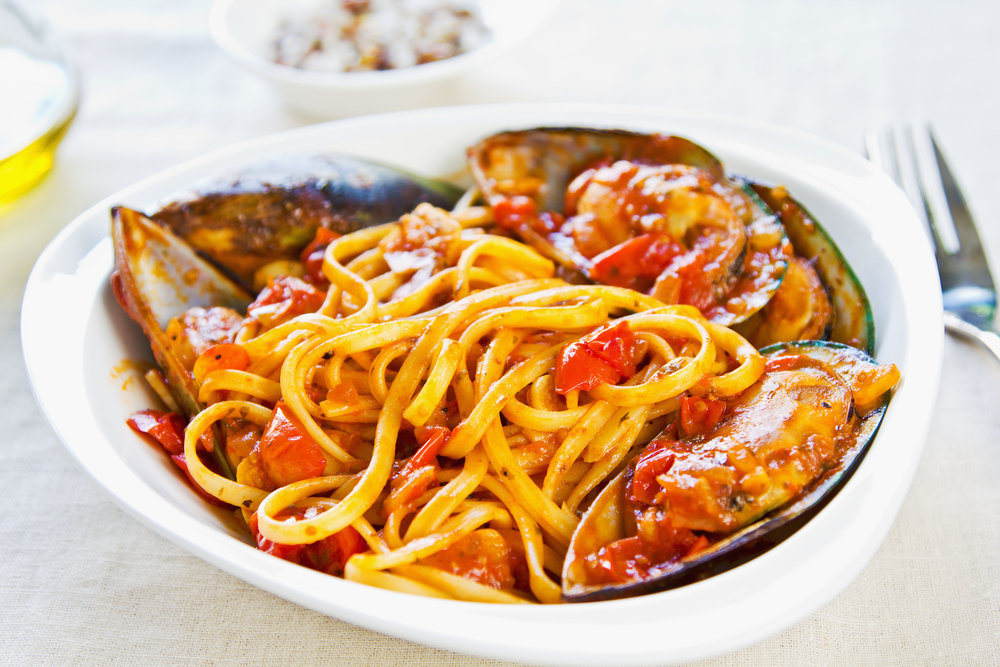 a pasta with red sauce with mussels and zucchini