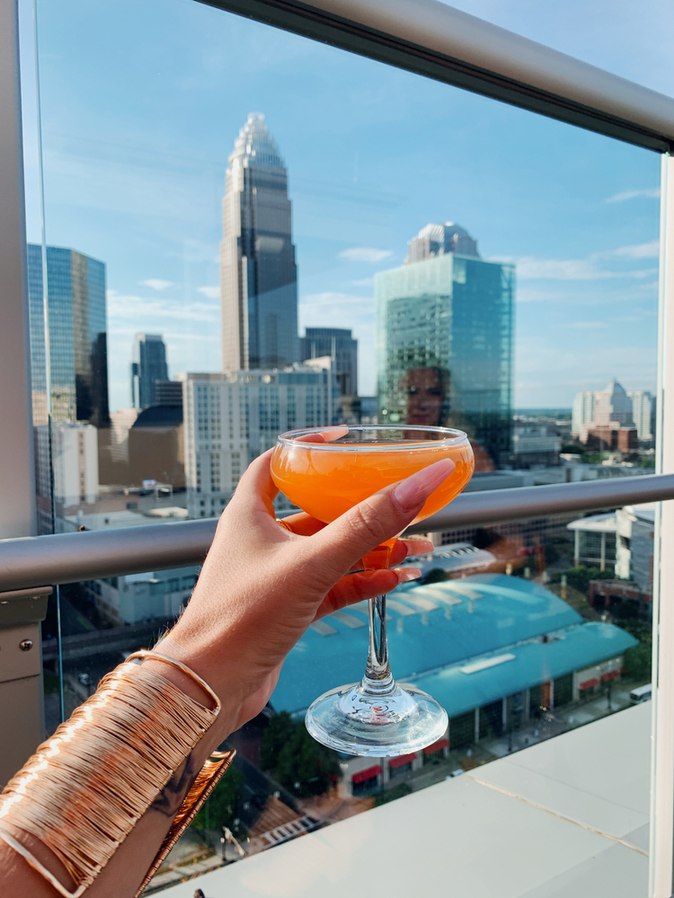 an orange cocktail being held up with the view of Charlotte in the background 
