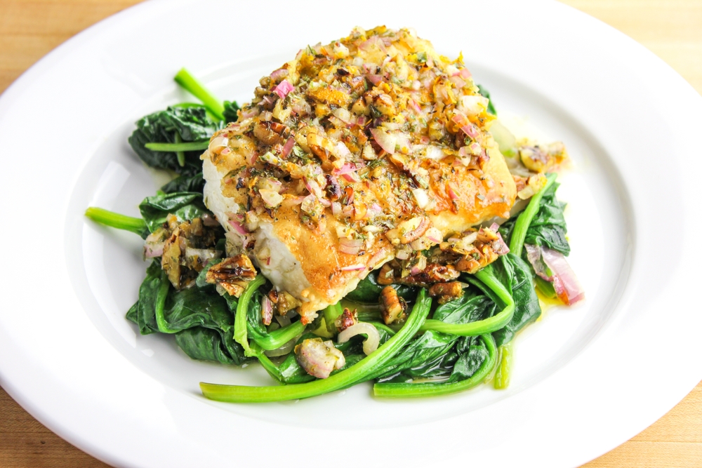 a pan seared trout with chopped pecans over a bed of wilted spinach