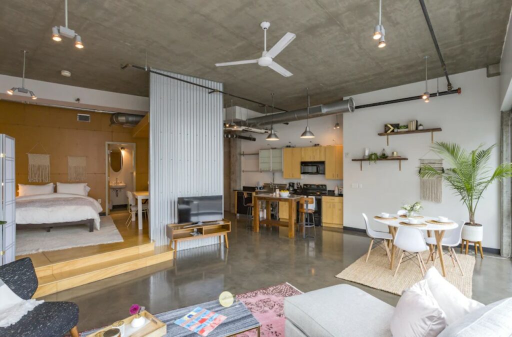 The inside of a loft that is perfect for staying in during a weekend in Nashville. It has a partitioned off bedroom, a couch, a dining table, and a kitchen. 