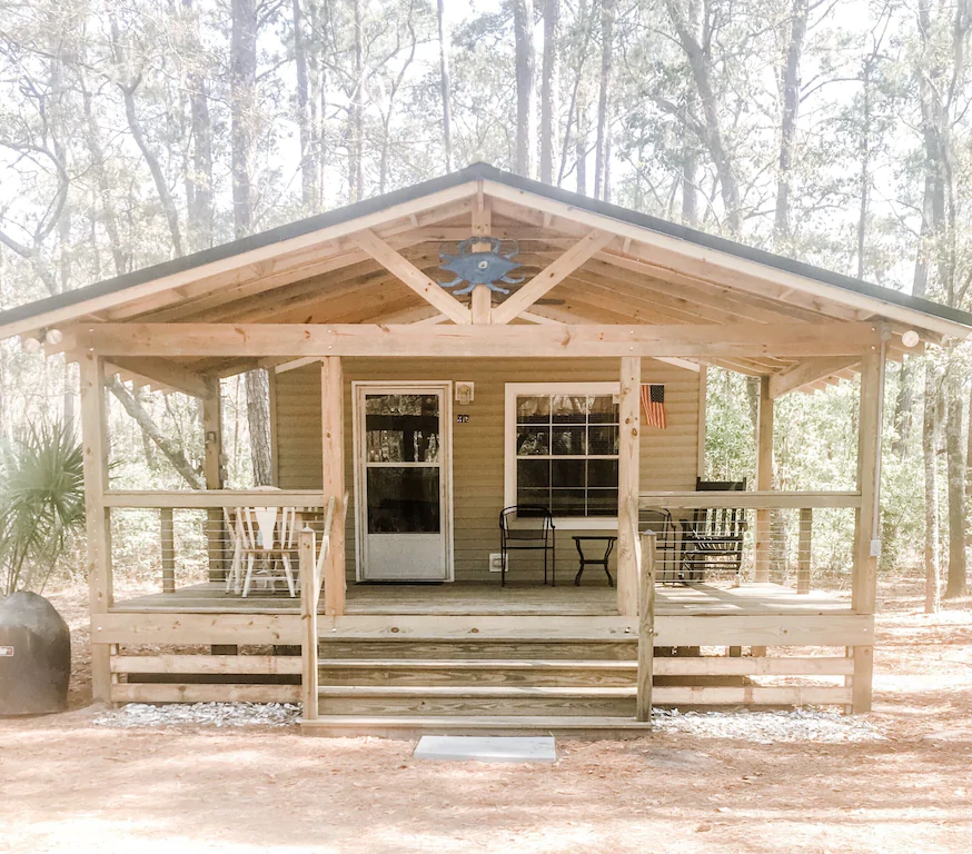 A wooden cabin with a large porch in the woods 