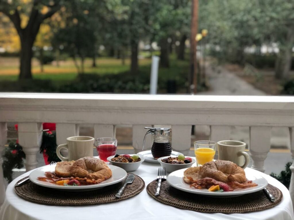 A breakfast including bacon and croissants sits on the balcony of a room at Forsyth Park Inn, one of the best boutique hotels in Savannah.