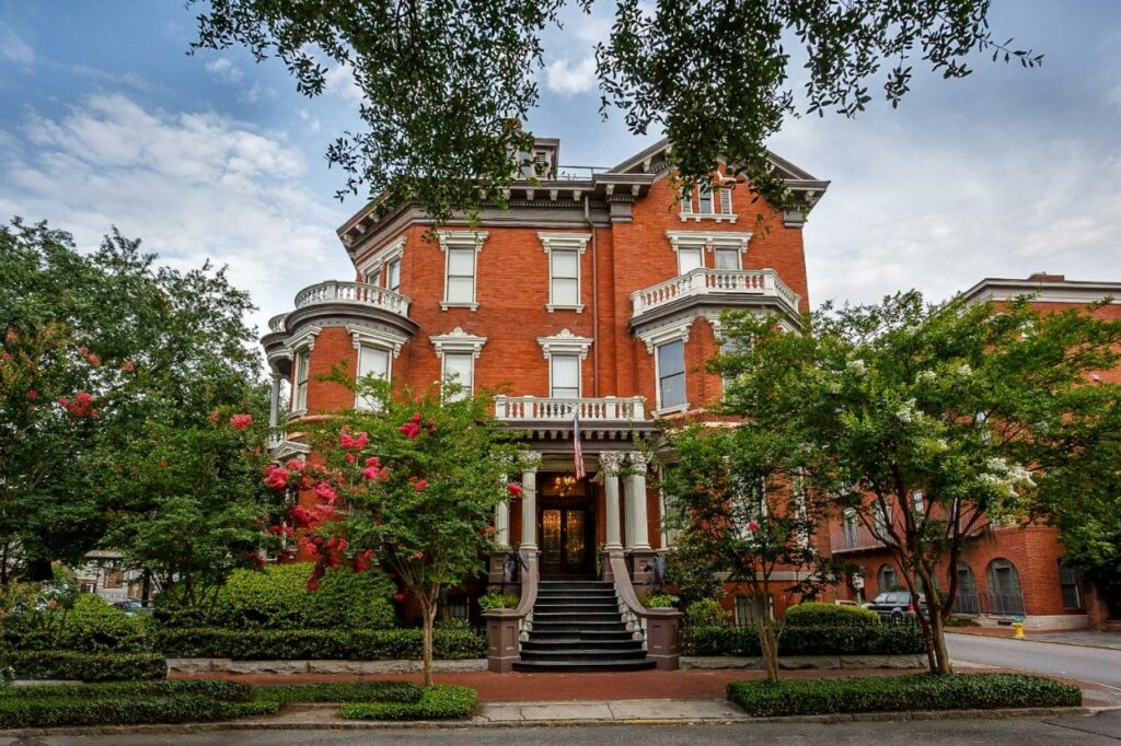 The red brick exterior of the Kehoe House, one of the most romantic boutique hotels in Savannah, sitting on a tree-lined street.