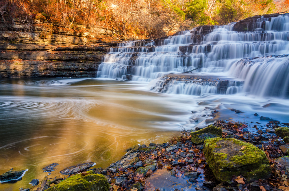 One of the waterfalls in Burgess Falls State Park flowing over small ledges into a pool on a fall day.