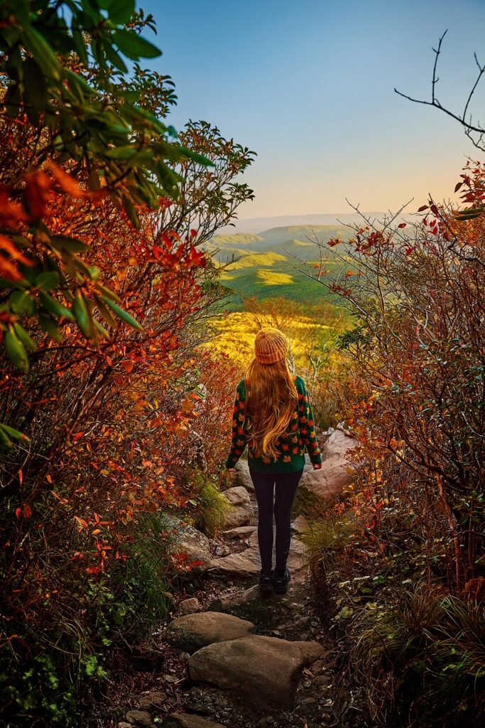 A woman in a sweater walking along a stone path surrounded by fall foliage.