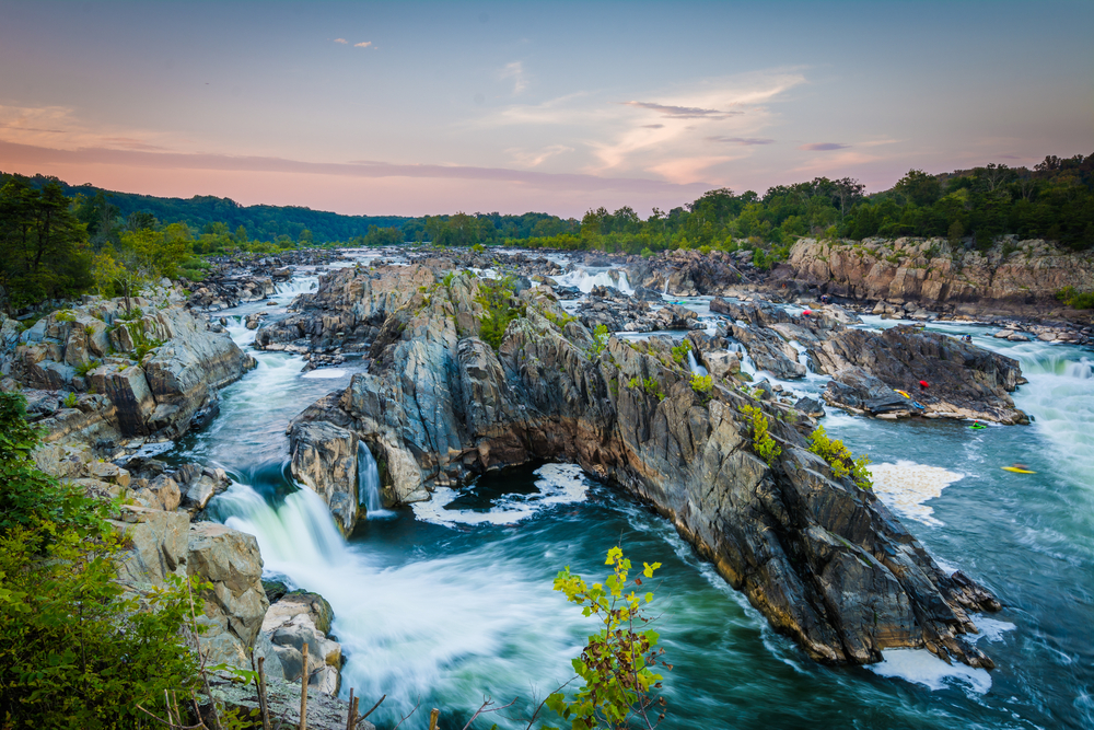 Sunset over the rugged waterfalls of Great Falls Park with kayakers in the water.