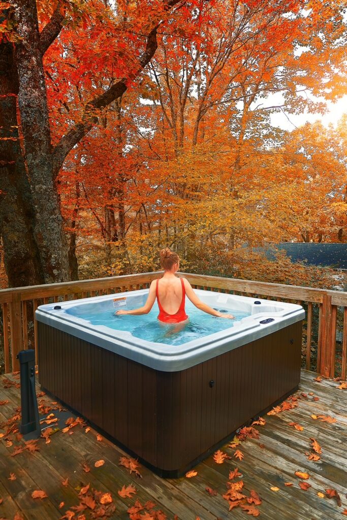 A woman stands in a hot tub on a deck overlooking red fall foliage.