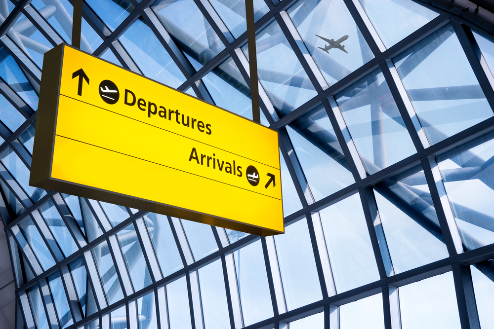 A yellow sign in an airport terminal that says 'Departures' and 'Arrivals'