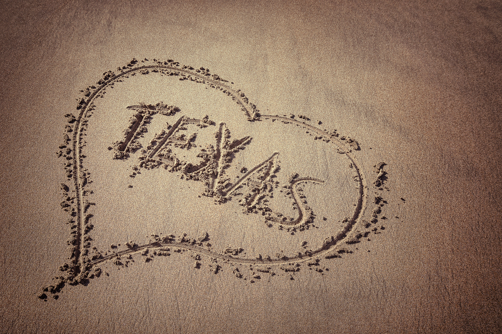 Photo of "Texas" written in the sand with a heart around it. 