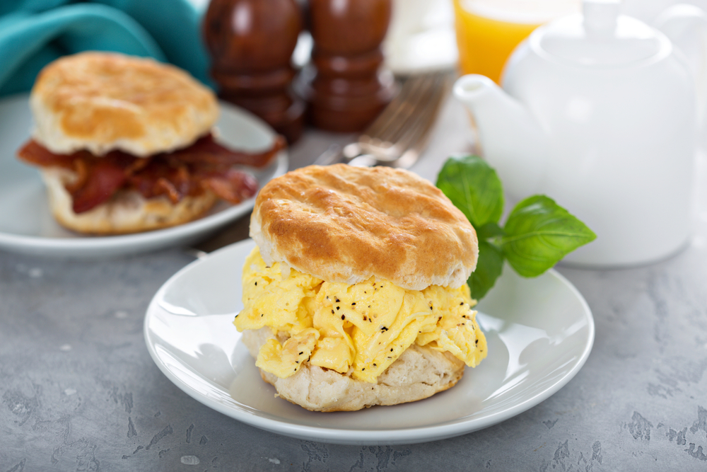 Breakfast biscuits with soft scrambled eggs and bacon on white plate in an article about the best breakfast in Louisville