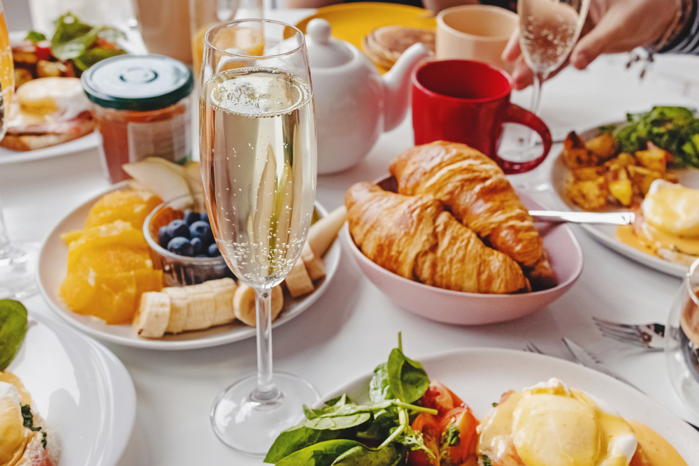 Glass of champagne close-up on the table with different breakfast and brunch dishes like croissants, eggs benedict, coffee and fruits. Brunches in Louisville are a great breakfast alternative 