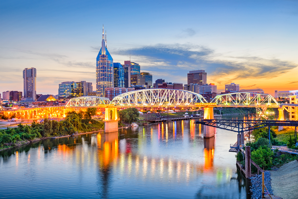 photo of the Nashville skyline at sunset, with a lighted bridge over water 
