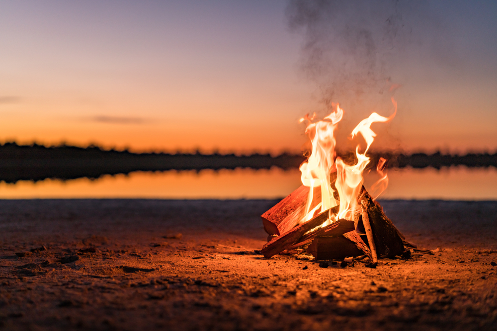 photo of a campfire off the lake at dusk 