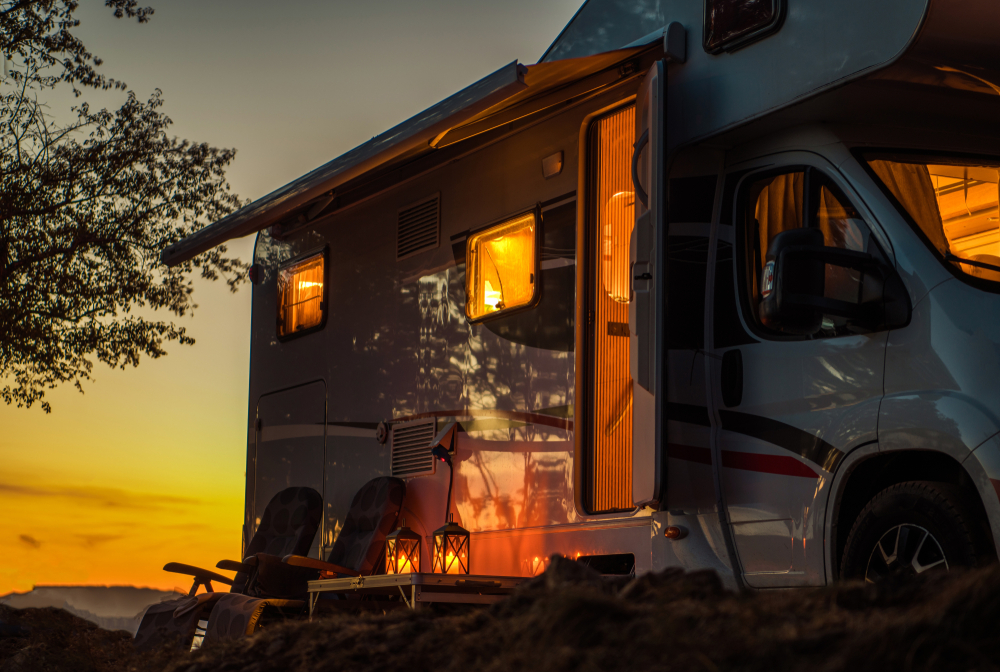 photo of an RV with two lit lanterns and two chairs in front of it at sunset 
