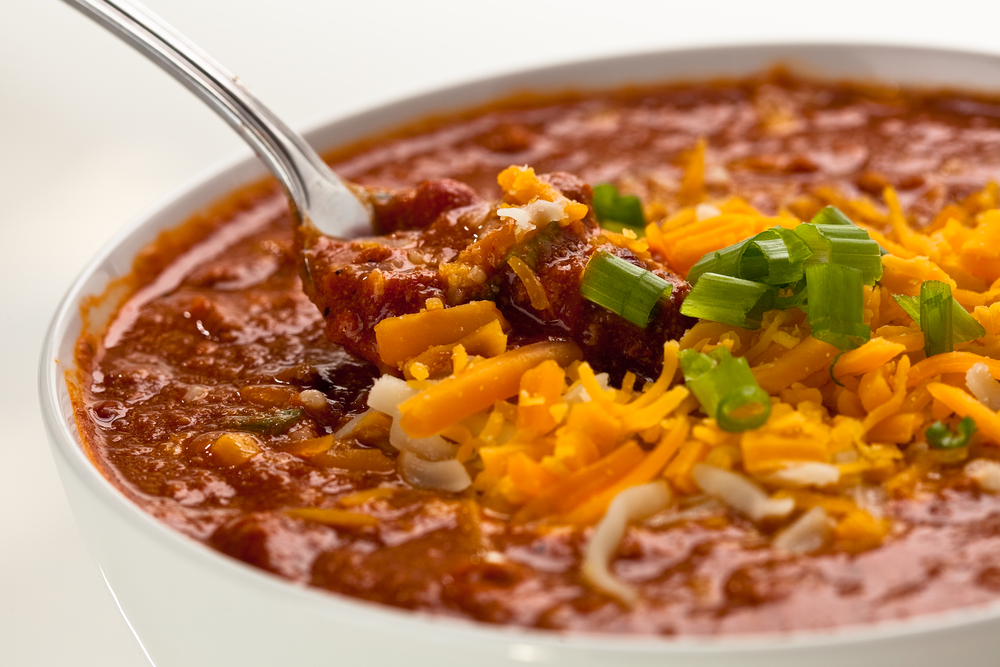 bowl of chilli with a spoon in it topped with cheese and green onions