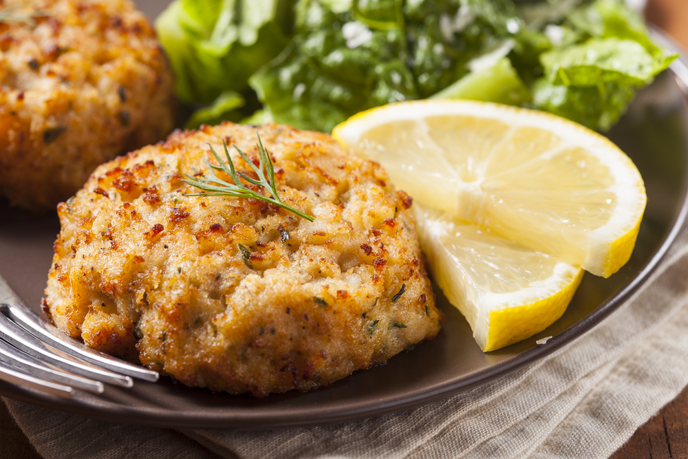 fried crab cakes on a plat with a lemon and salad