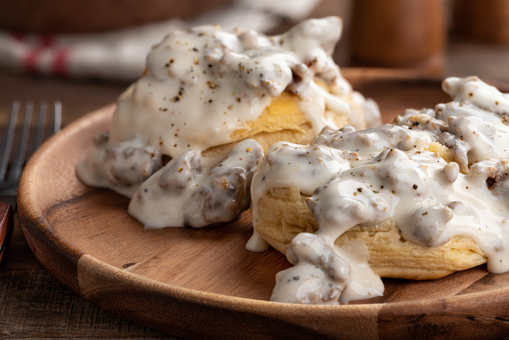 Biscuits on a wooden plate covered in gravy in an article about restaurants in Louisville 