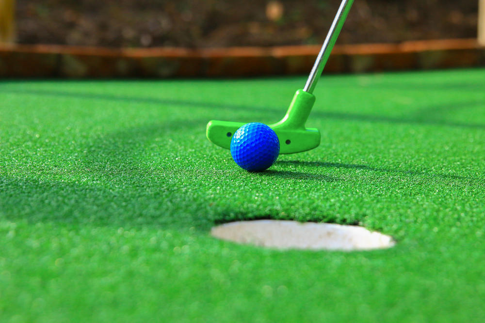 a mini golf club putting a golf ball into a hole in the ground