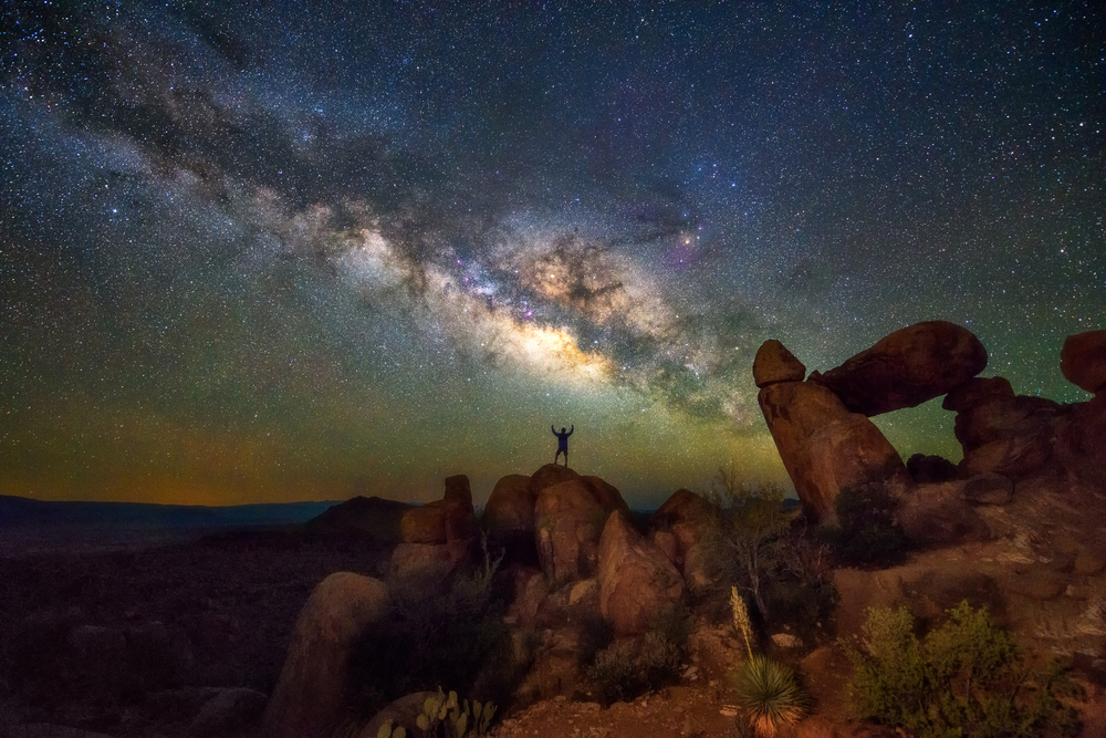 A man standing on the rocks at Big Bend national park with the starry night sky