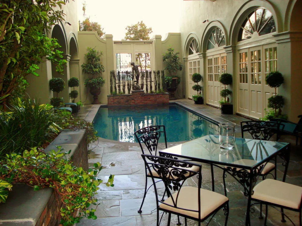 a great pool with classic dark features, greenery and arched windows accent this outdoor courtyard featured at Beinville, one of the New Orleans haunted hotels